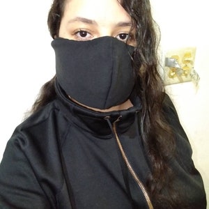 Puede incluir: Una persona con una camisa negra de cuello alto con cremallera y una máscara facial negra.
