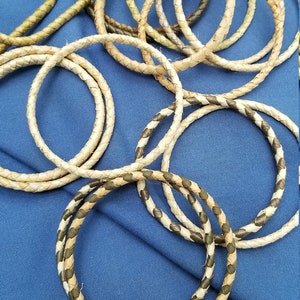 May include: A collection of braided leather cords in various shades of brown and green. The cords are arranged in a circular pattern on a blue background.