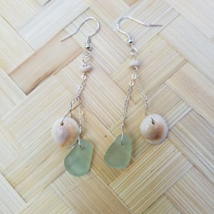 May include: A pair of long, silver dangle earrings with a light brown bead, a light brown seashell, and a light green sea glass charm on each earring.