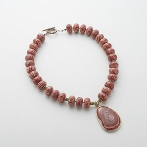 May include: A red and white striped stone bead necklace with a matching pendant. The necklace has a silver clasp.