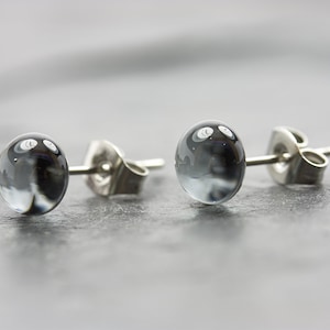 May include: A pair of silver stud earrings with round, clear glass stones that have a swirling, grey pattern inside.
