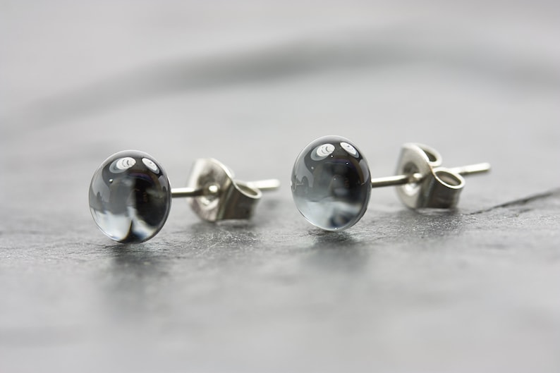 May include: A pair of silver stud earrings with round, clear glass stones that have a swirling, grey pattern inside.