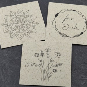 May include: Three blank cards with different black line drawings. The first card has a stylised flower, the second card has a wreath with the text "f&uuml;r Dich" inside, and the third card has a bouquet of flowers.