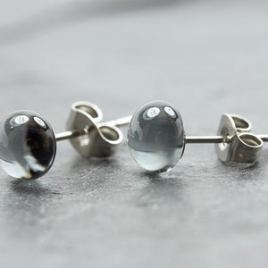 May include: A pair of silver stud earrings with round, clear glass beads. The beads have a swirling, cloudy pattern.