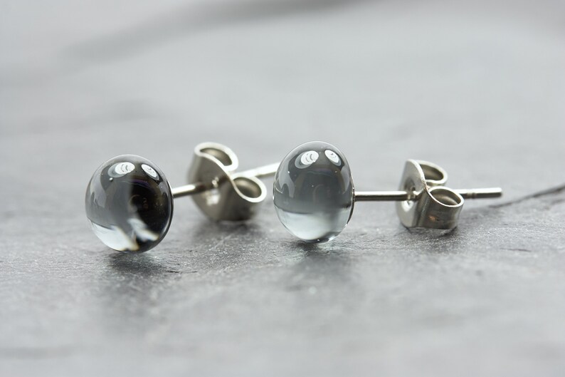May include: A pair of silver stud earrings with round, clear glass beads. The beads have a swirling, cloudy pattern.