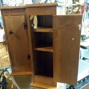 May include: Two wooden cabinets with doors and shelves. The cabinets are stained a dark brown color and have a simple design. The cabinets are sitting on a metal surface.