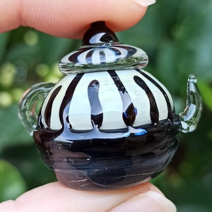 May include: A small, black and white striped glass teapot with a clear glass lid. The teapot is about the size of a thumb.