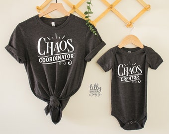 May include: A dark gray t-shirt with the text "Chaos Coordinator" in white lettering. Next to it is a dark gray baby onesie with the text "Chaos Creator" in white lettering.