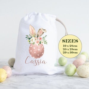 May include: White fabric gift bag featuring a pink and white bunny and egg design. The bag is personalised with the name "Cassia". Available in three sizes: 19 x 28cm, 25 x 28cm, and 29 x 39cm.