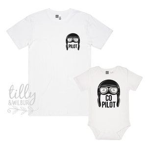May include: White t-shirt with the word "PILOT" and a graphic of a pilot's helmet with goggles. A white baby onesie with the words "CO PILOT" and a graphic of a pilot's helmet with goggles.