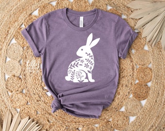 May include: A purple t-shirt with a white floral bunny design. The bunny is outlined in white and filled with white floral details.