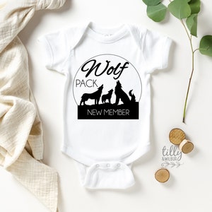 May include: White baby onesie with a black circle graphic featuring three wolf silhouettes and the text "Wolf Pack New Member".