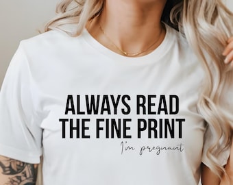 Może przedstawiać: Biała koszulka z napisem "ALWAYS READ THE FINE PRINT" pogrubionymi czarnymi literami. Poniżej, kursywą, napis "I'm pregnant". Koszulka ma swobodny styl.