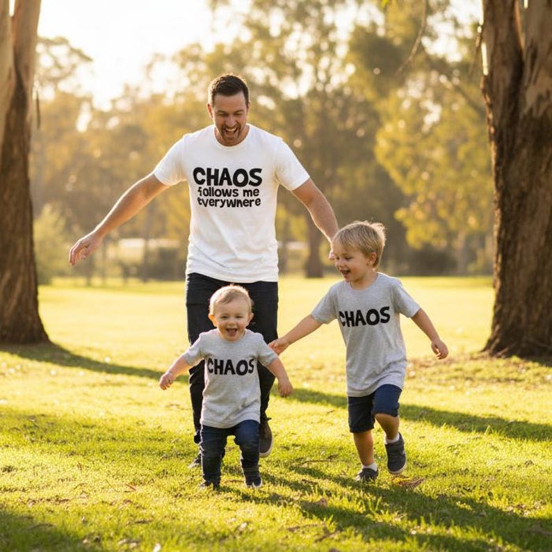 Tilly&Wilbur matching set — a white adult tee reading "Chaos Follows Me Everywhere" and grey t-shirts reading "Chaos" in bold rounded lettering, worn by a dad and two children playing outdoors