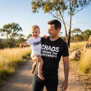 Tilly&Wilbur matching set — a black adult tee reading "Chaos Follows Me Everywhere" and a white baby bodysuit reading "Chaos" in bold rounded lettering, worn by a dad holding his laughing baby outdoors.