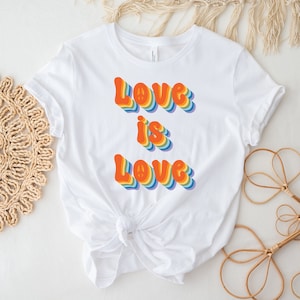 May include: White t-shirt featuring a rainbow-coloured graphic that reads "Love is Love" in a retro font.