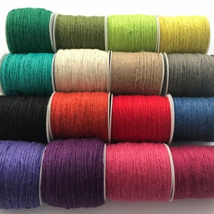 May include: A collection of 15 spools of twine in various colours, including green, white, brown, grey, black, orange, red, blue, purple, and pink. The twine is wound around spools with white centres.