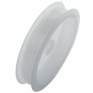 May include: A spool of clear elastic thread for jewelry making. The thread is wound around a white plastic spool.