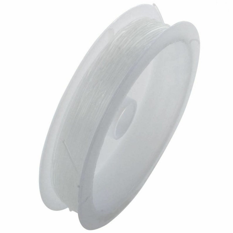 May include: A spool of clear elastic thread for jewelry making. The thread is wound around a white plastic spool.