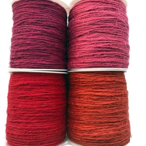 May include: Four spools of twine in various shades of red and pink. The twine is wound around white cardboard spools.