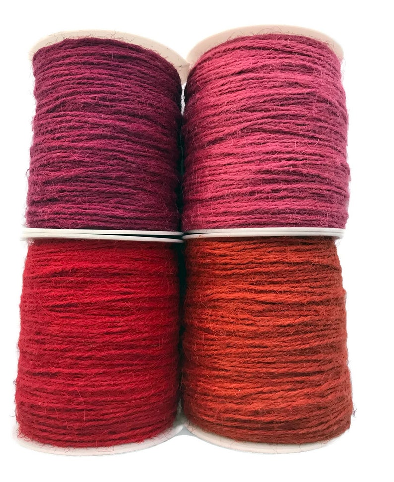 May include: Four spools of twine in various shades of red and pink. The twine is wound around white cardboard spools.