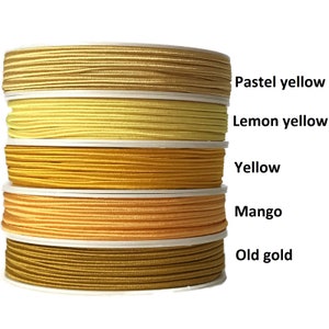Peut inclure: Cinq bobines de cordon élastique dans différentes nuances de jaune, du jaune pâle à l'or. Les bobines sont étiquetées "Jaune pastel", "Jaune citron", "Jaune", "Mangue" et "Or vieil".