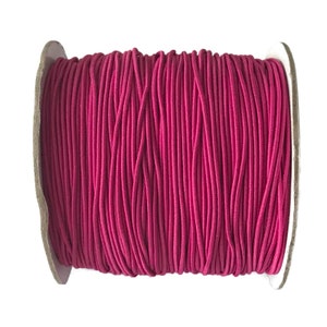 May include: A spool of pink elastic cord, wound tightly on a cardboard core.