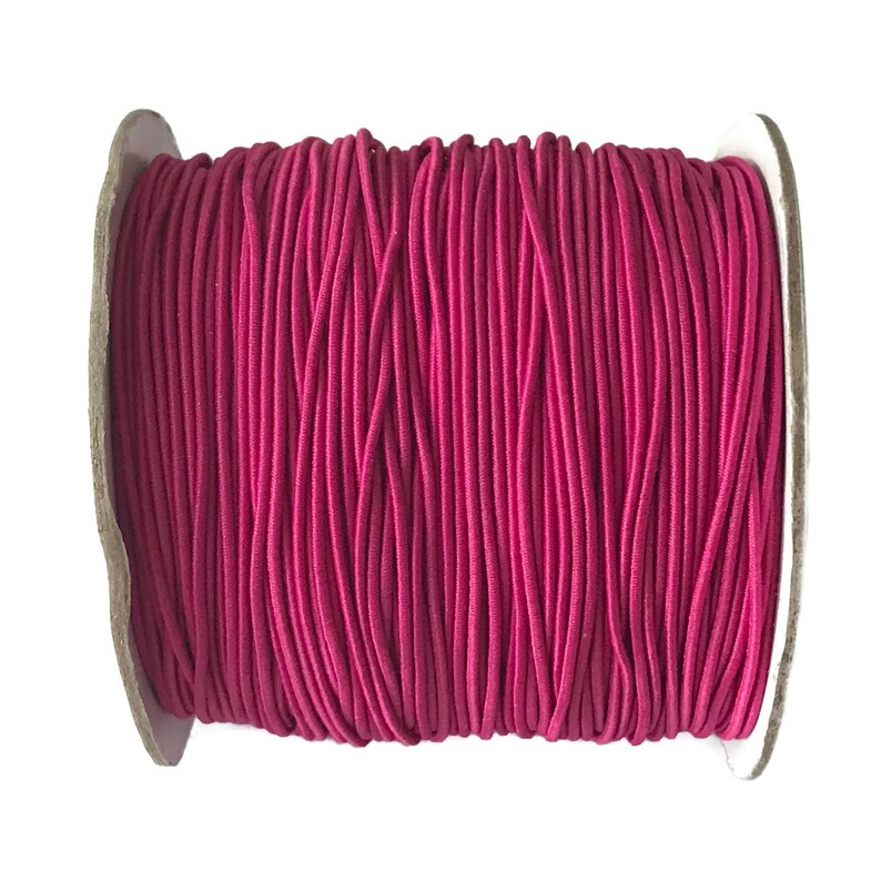 May include: A spool of pink elastic cord, wound tightly on a cardboard core.