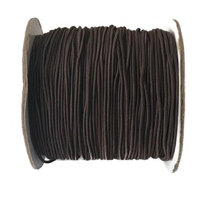 May include: A spool of brown elastic cord. The cord is wound tightly around a cardboard spool.