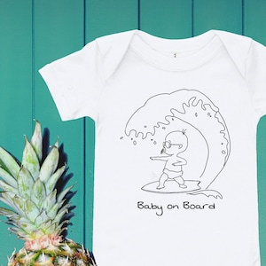 May include: White babygrow with a black line drawing of a baby surfing on a wave. The text "Baby on Board" is printed below the image.