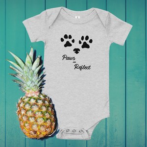 May include: A grey baby onesie with black paw prints and the text "Paws and Reflect".