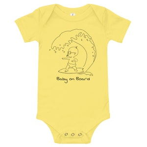 May include: A yellow babygrow with a black line drawing of a baby wearing sunglasses and surfing on a wave. The text "Baby on Board" is printed below the image.