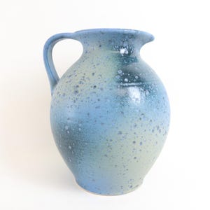 May include: A blue and green ceramic pitcher with a speckled glaze. The pitcher has a round body and a handle.