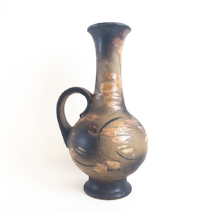 May include: A brown ceramic vase with a black handle and a floral design. The vase has a narrow neck and a rounded body.