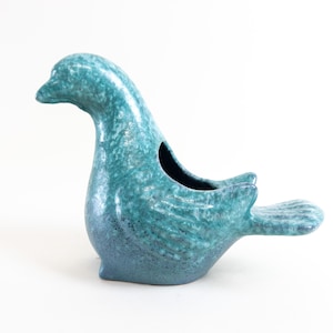 May include: A teal blue ceramic bird planter with a textured finish. The bird has a long neck and a small opening in its back for planting.