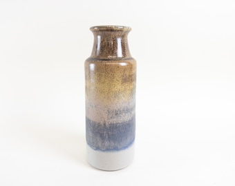 Könnte beinhalten: Eine Keramikvase mit brauner, gelber und blauer Glasur. Die Vase hat eine zylindrische Form und einen schmalen Hals.