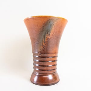 以下が含まれることがあります： 茶色いセラミックの花瓶で、開口部が広く、底がリブ状になっています。花瓶は、茶色、オレンジ、グレーの色の斑点のある釉薬がかかっています。