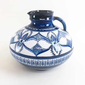 May include: A blue and white ceramic pitcher with a floral design. The pitcher has a wide base and a narrow neck.