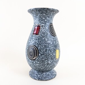 Puede incluir: Un jarrón de cerámica gris con un acabado moteado y diseños geométricos abstractos en negro, rojo y amarillo.