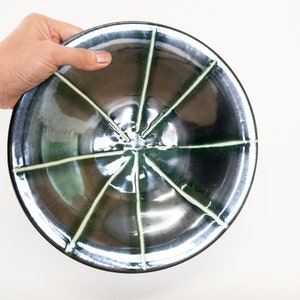 May include: A black ceramic bowl with a green glaze and white lines radiating from the center. The bowl is slightly curved and has a glossy finish.