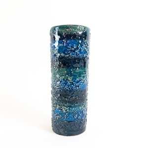 May include: A tall, cylindrical ceramic vase with a blue and green glaze. The glaze has a textured, speckled appearance, creating a unique and artistic look.