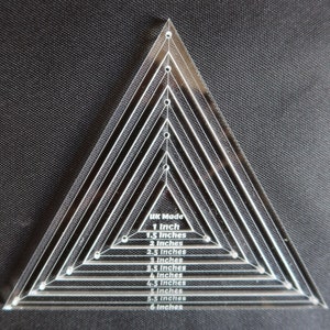 May include: A clear acrylic triangle ruler with markings for 1, 1.5, 2, 2.5, 3, 3.5, 4, 4.5, 5, 5.5, and 6 inches. The ruler is labeled "UK Made".