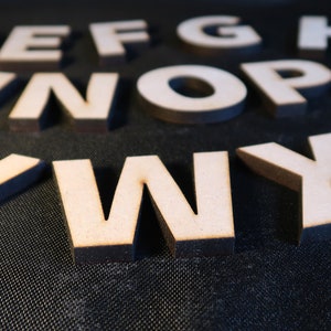 May include: Wooden letters of the alphabet, painted white, are scattered on a black surface. The letters are in various sizes and are arranged in a random pattern.