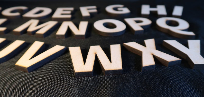 May include: Wooden letters of the alphabet, painted white, are scattered on a black surface. The letters are in various sizes and are arranged in a random pattern.