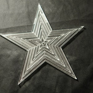 May include: A clear plastic star-shaped template with a layered design. The star is made of multiple lines that create a geometric pattern.