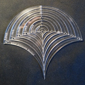 Op de afbeelding: Een transparante plastic sjabloon met 10 aflopende halve cirkelvormen, variërend in grootte van 2,5 cm tot 15 cm. De sjabloon is gelabeld "Paul Williams Design".