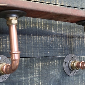 Peut inclure: Deux étagères en cuivre avec des brides en fer noir et des raccords en laiton montés sur une planche de bois rustique.