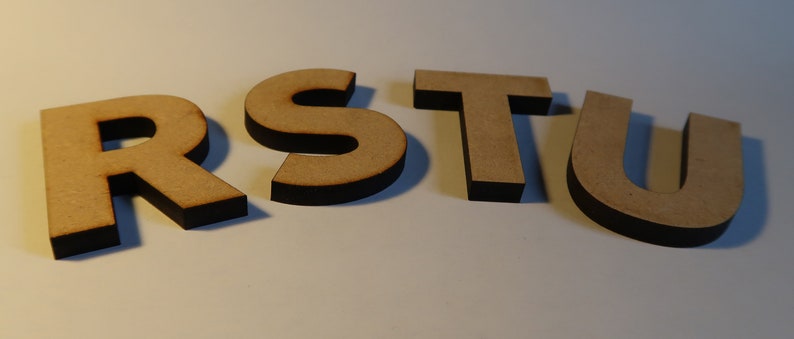 May include: Wooden letters spelling out the word "RSTU" in a light brown color with black edges.
