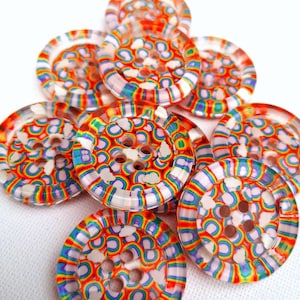 Pode incluir: Um grupo de botões coloridos do arco-íris com nuvens brancas e um acabamento de plástico transparente. Os botões têm quatro furos cada.