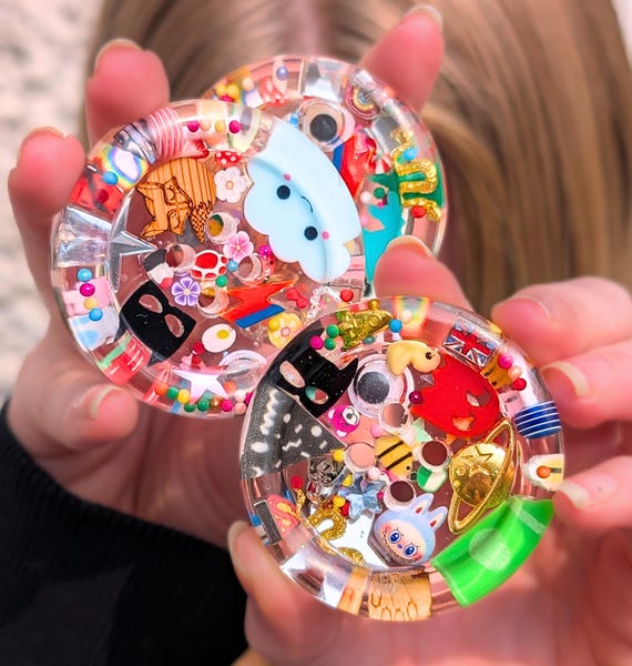A 50mm giant resin-cast button with a hyper-detailed eyeball inside — absurdly specific object that doubles as a fidget toy, collage prop, or shelf curiosity.